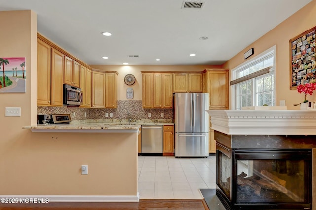 kitchen featuring light stone counters, stainless steel appliances, visible vents, and decorative backsplash