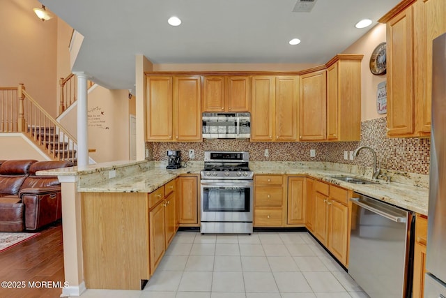 kitchen with light stone counters, light tile patterned floors, appliances with stainless steel finishes, a peninsula, and a sink