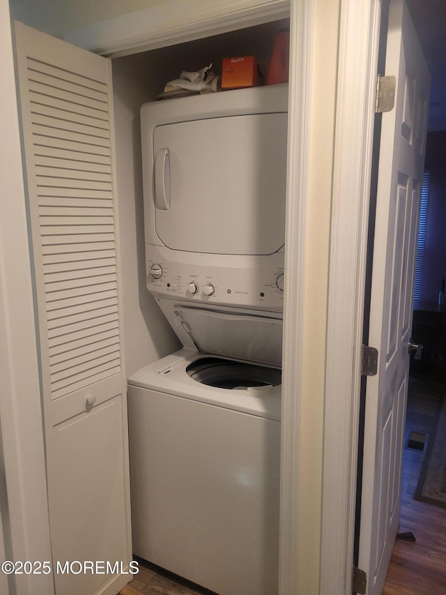 laundry room with dark hardwood / wood-style floors and stacked washing maching and dryer