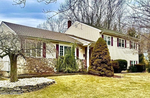 view of front facade featuring a front yard, a chimney, and a shingled roof