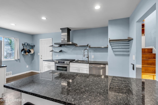 kitchen with appliances with stainless steel finishes, white cabinetry, sink, dark wood-type flooring, and wall chimney exhaust hood