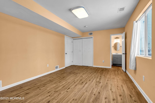 unfurnished bedroom featuring sink, ensuite bath, light hardwood / wood-style floors, and a closet