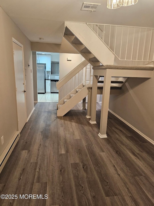 stairs featuring baseboard heating, wood finished floors, visible vents, and baseboards