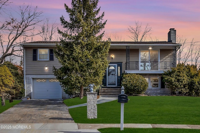 bi-level home with a front yard, decorative driveway, a chimney, and an attached garage