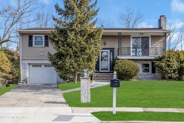 split foyer home with decorative driveway, a chimney, a balcony, a garage, and a front lawn