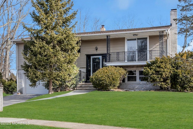 bi-level home featuring a chimney, a balcony, a garage, driveway, and a front lawn