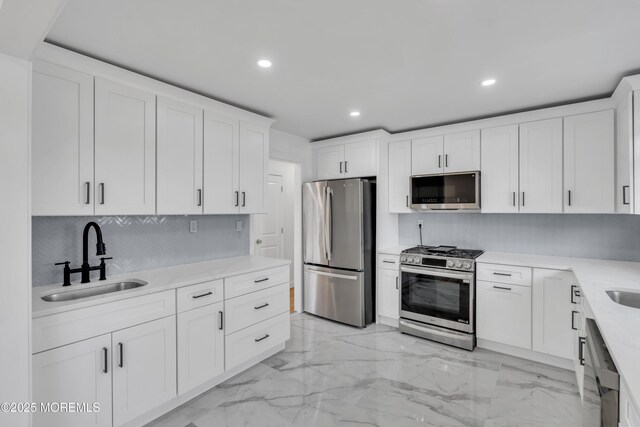 kitchen featuring appliances with stainless steel finishes, marble finish floor, light countertops, white cabinetry, and a sink