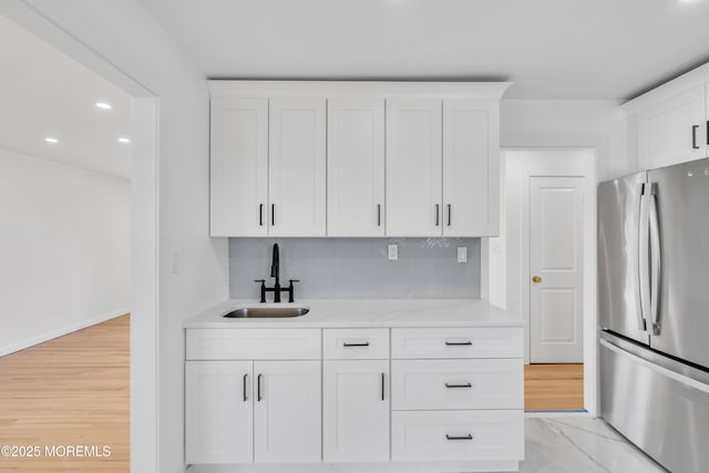 kitchen featuring decorative backsplash, white cabinets, freestanding refrigerator, marble finish floor, and a sink