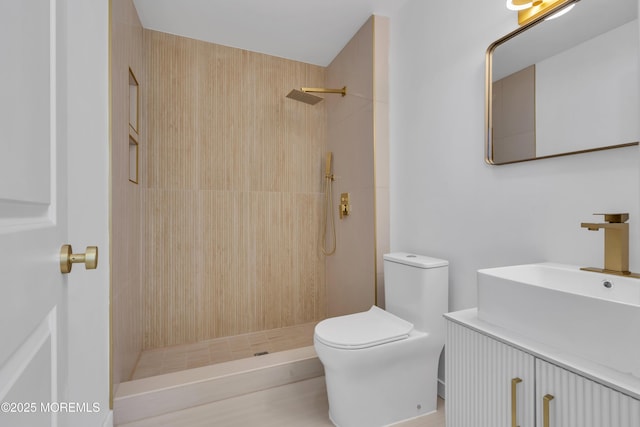 bathroom with toilet, a tile shower, and vanity