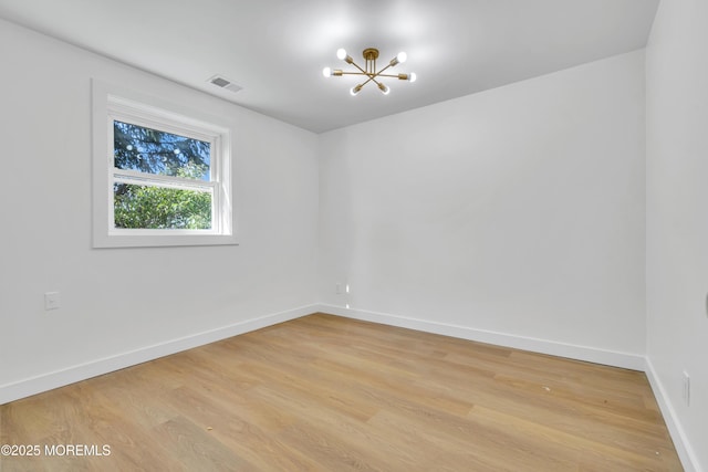 empty room featuring a chandelier, light wood-type flooring, visible vents, and baseboards