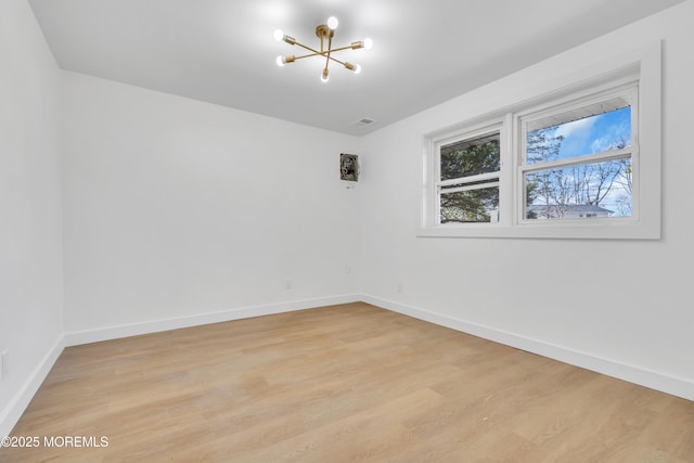 spare room with a chandelier, light wood-style flooring, and baseboards