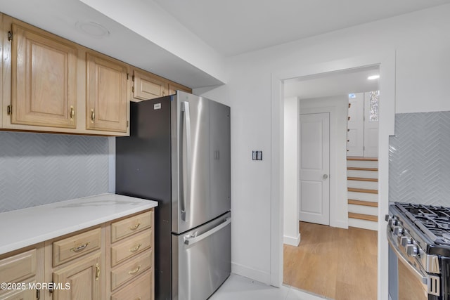 kitchen featuring tasteful backsplash, light brown cabinetry, appliances with stainless steel finishes, light wood-style floors, and baseboards