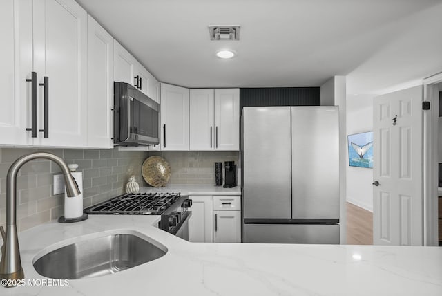 kitchen with appliances with stainless steel finishes, sink, white cabinets, and light stone counters