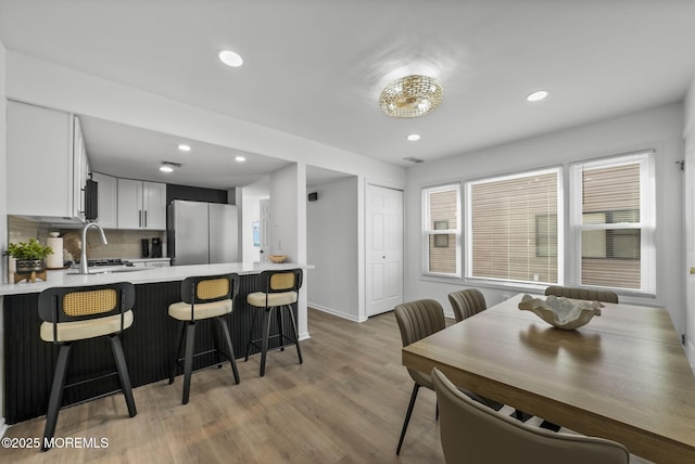 kitchen featuring white cabinetry, light hardwood / wood-style flooring, a kitchen breakfast bar, stainless steel fridge, and kitchen peninsula