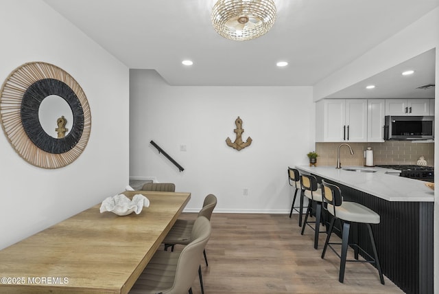 kitchen with white cabinetry, sink, backsplash, light hardwood / wood-style floors, and light stone countertops