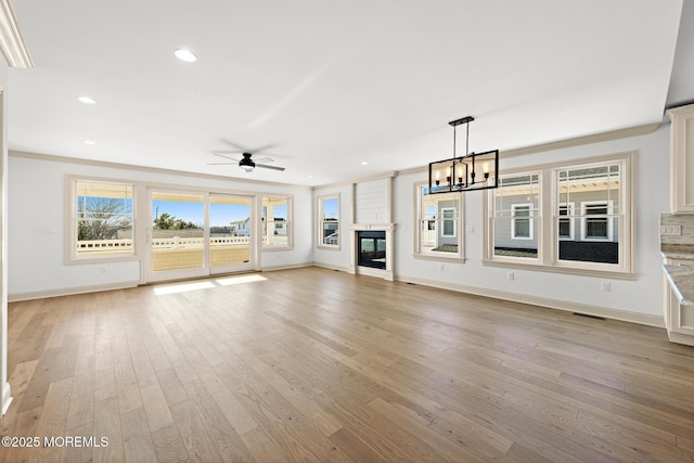 unfurnished living room featuring ceiling fan with notable chandelier, ornamental molding, a large fireplace, and light wood-type flooring