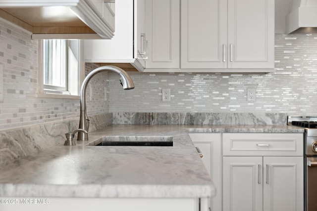 kitchen with sink, white cabinetry, light stone counters, tasteful backsplash, and extractor fan