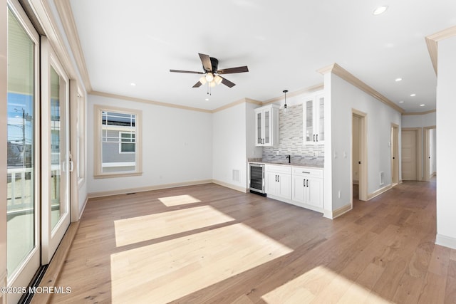 unfurnished living room with ornamental molding, bar, beverage cooler, and light wood-type flooring