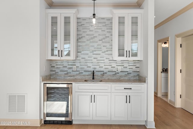 bar with sink, hanging light fixtures, beverage cooler, light stone countertops, and white cabinets