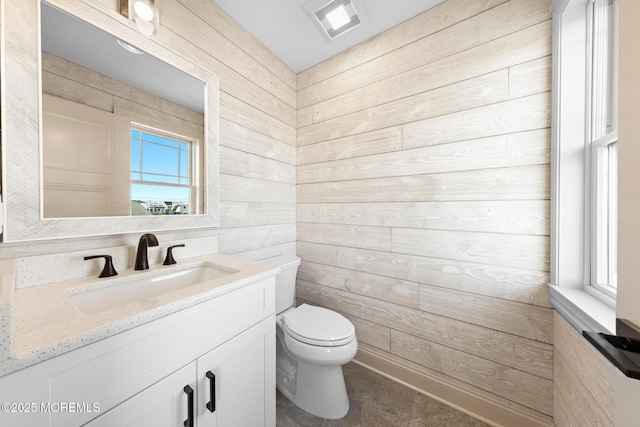 bathroom featuring vanity, wooden walls, and toilet