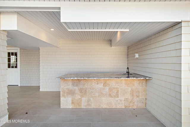 exterior space with tile patterned floors, light stone countertops, and tile walls