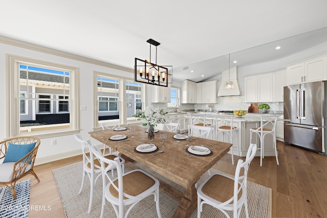 dining space with lofted ceiling, sink, light hardwood / wood-style floors, and an inviting chandelier