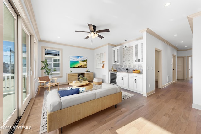 living room with crown molding, bar area, beverage cooler, and light wood-type flooring