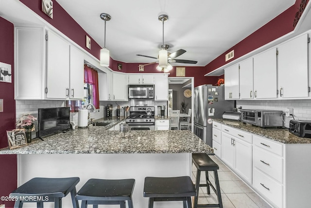 kitchen with a breakfast bar area, white cabinetry, stainless steel appliances, decorative backsplash, and kitchen peninsula