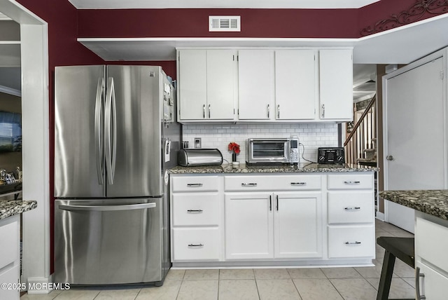 kitchen featuring stainless steel refrigerator, white cabinets, tasteful backsplash, and dark stone countertops