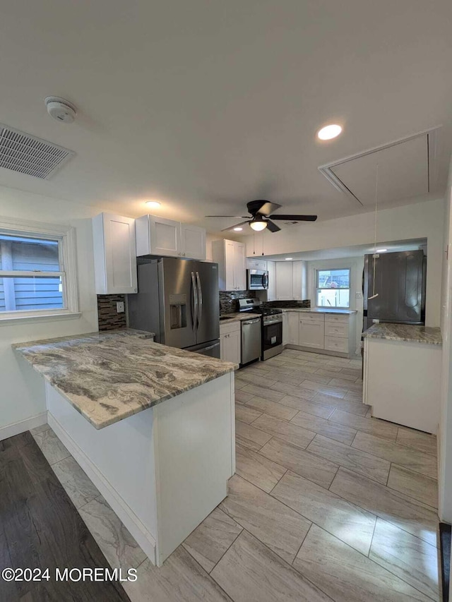 kitchen with white cabinetry, decorative backsplash, kitchen peninsula, stainless steel appliances, and light stone countertops