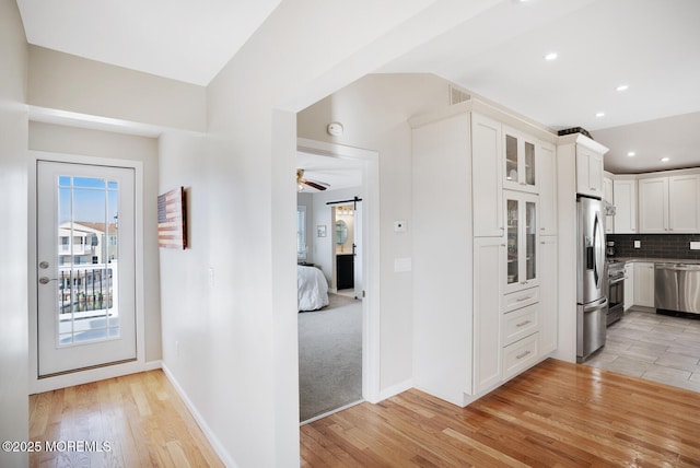 kitchen with stainless steel appliances, white cabinets, decorative backsplash, a barn door, and light wood-type flooring