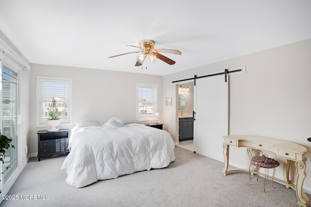 carpeted bedroom with a barn door, ceiling fan, and ensuite bathroom