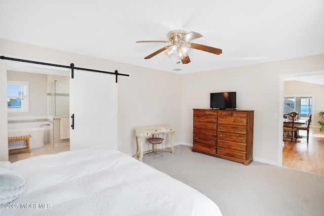 carpeted bedroom featuring ceiling fan, a barn door, and ensuite bath