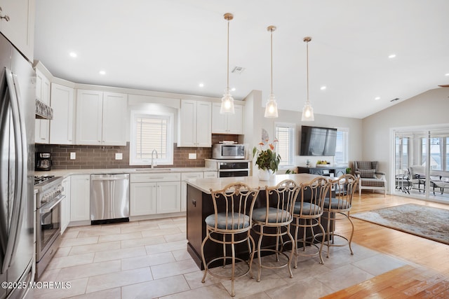 kitchen featuring white cabinetry, hanging light fixtures, appliances with stainless steel finishes, a kitchen breakfast bar, and a kitchen island