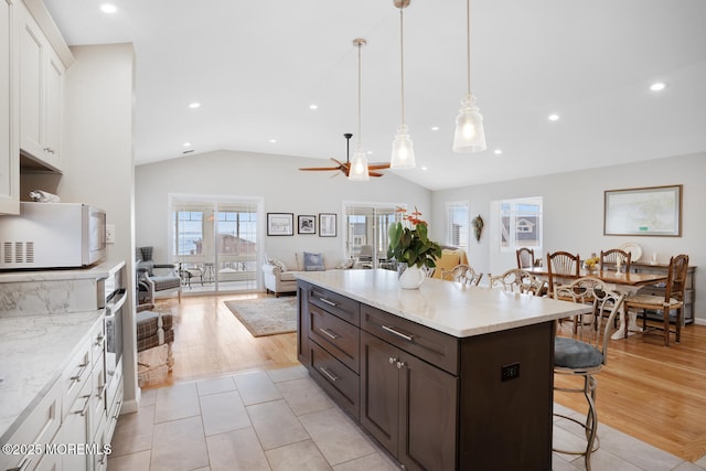 kitchen with dark brown cabinetry, vaulted ceiling, hanging light fixtures, a kitchen breakfast bar, and white cabinets