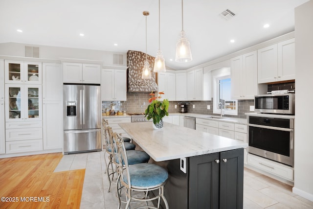 kitchen featuring white cabinetry, decorative light fixtures, a kitchen island, and appliances with stainless steel finishes