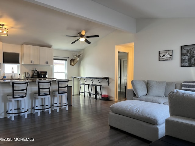 living room with lofted ceiling with beams, dark wood-type flooring, sink, and ceiling fan