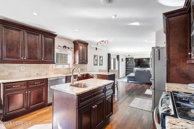 kitchen featuring appliances with stainless steel finishes, tasteful backsplash, sink, dark hardwood / wood-style flooring, and a kitchen island with sink