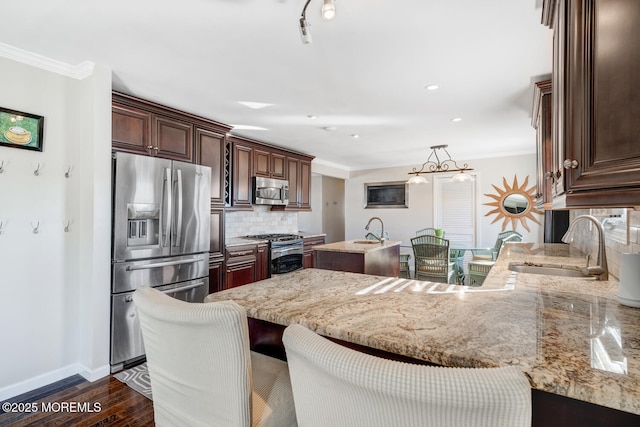 kitchen featuring dark wood-type flooring, crown molding, decorative light fixtures, appliances with stainless steel finishes, and backsplash