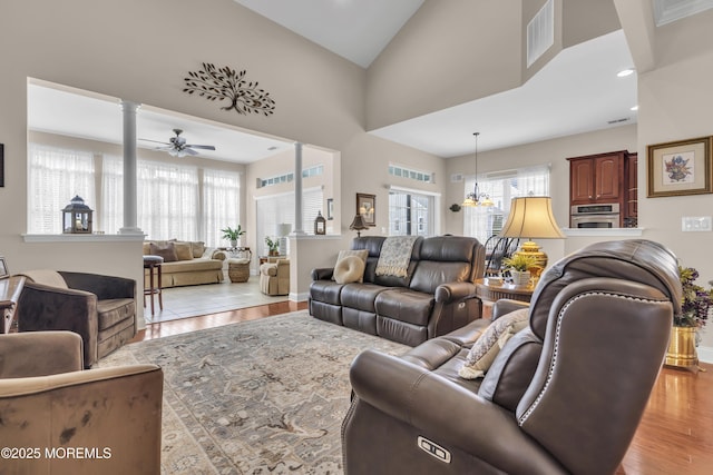 living room featuring a towering ceiling, decorative columns, ceiling fan, and light wood-type flooring