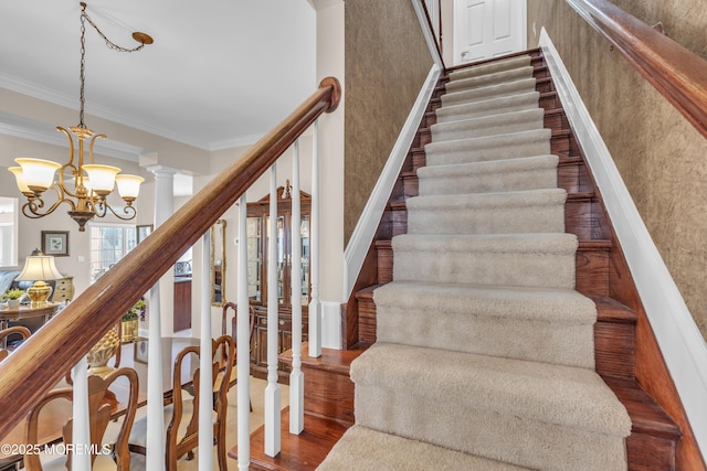 stairway featuring hardwood / wood-style flooring, a notable chandelier, ornamental molding, and ornate columns