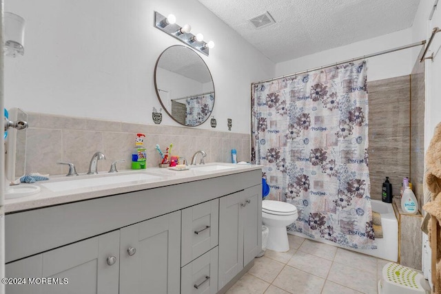 full bathroom with toilet, a textured ceiling, tile walls, vanity, and tile patterned flooring