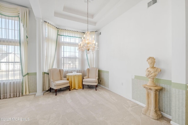 sitting room featuring an inviting chandelier, decorative columns, a raised ceiling, and carpet