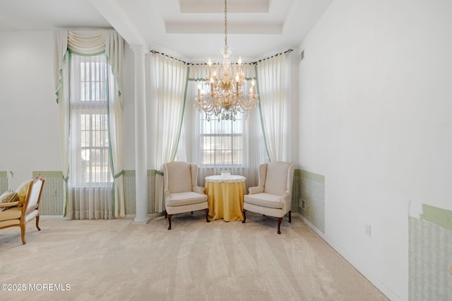 living area featuring light carpet, a tray ceiling, decorative columns, and an inviting chandelier