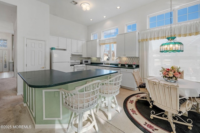 kitchen with a high ceiling, white cabinetry, hanging light fixtures, and white appliances