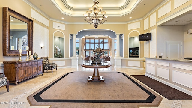 foyer with a towering ceiling, decorative columns, ornamental molding, a raised ceiling, and an inviting chandelier