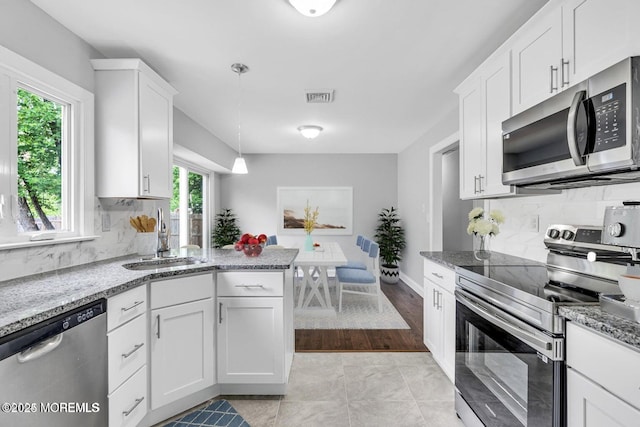 kitchen with appliances with stainless steel finishes, white cabinetry, a sink, and light stone countertops