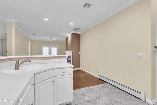 kitchen featuring baseboard heating, ornamental molding, sink, and white cabinets