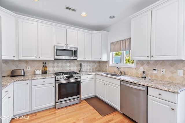 kitchen with appliances with stainless steel finishes, tasteful backsplash, white cabinetry, sink, and light hardwood / wood-style floors