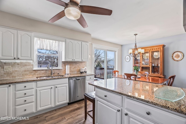 kitchen with sink, dishwasher, hanging light fixtures, light stone counters, and white cabinets